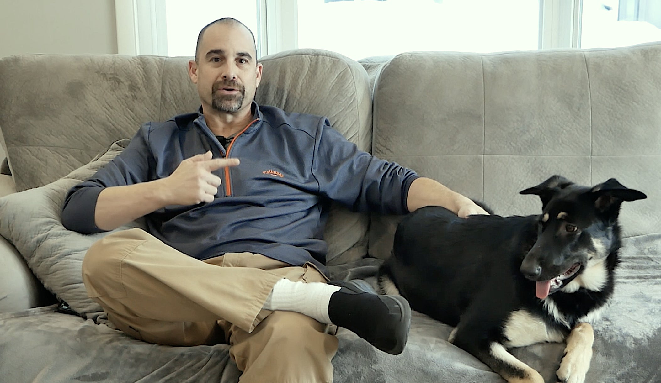 Man sitting on a gray couch with his dog, sharing a testimonial about removing pet odors using Blaze Away odor eliminator.