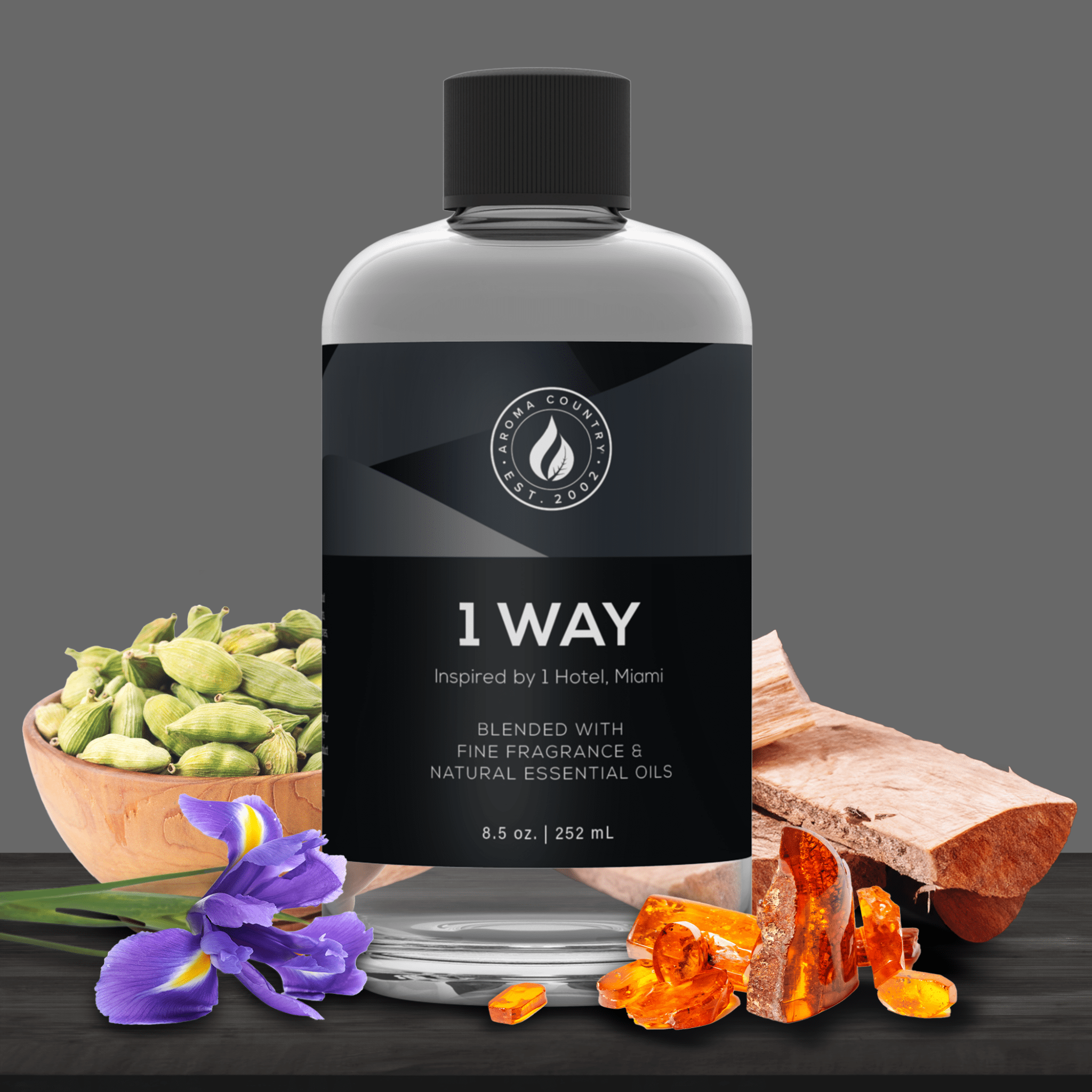 8.5 oz bottle of 1 Way diffuser oil inspired by 1 Hotel Miami, displayed with cardamom, iris flower, amber resin, and wood on a dark surface.