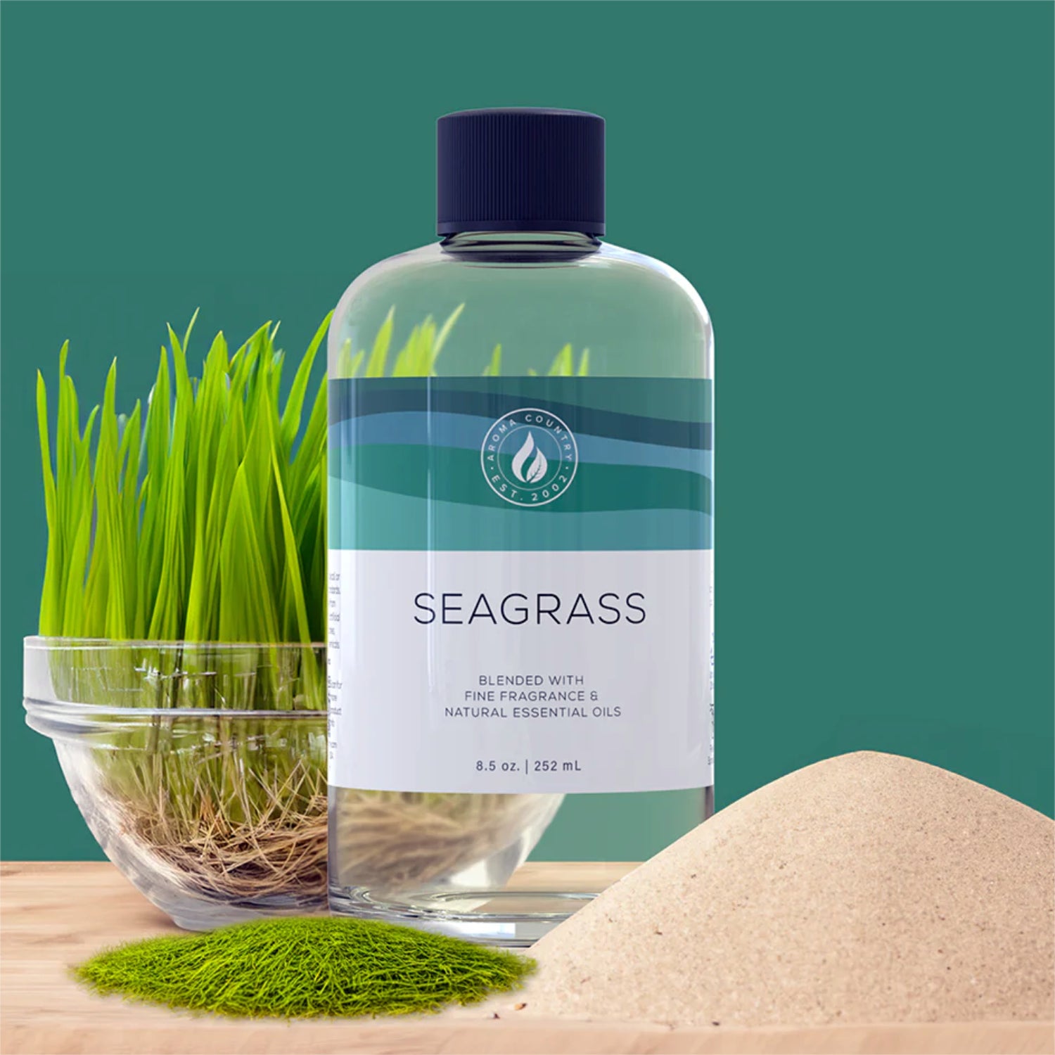 Seagrass diffuser oil bottle with fresh green seagrass, a sand mound, and aromatic moss accents for a coastal-inspired home fragrance.