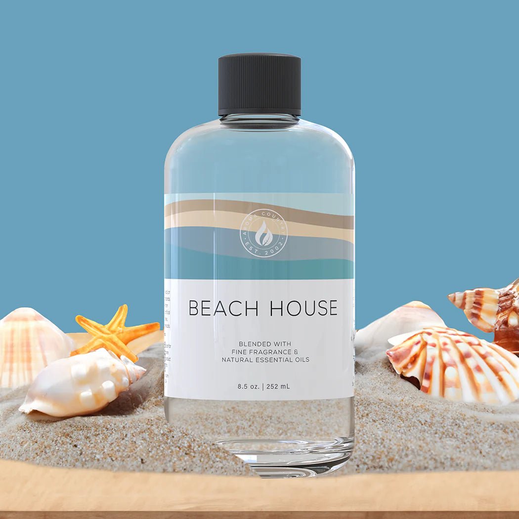 Beach House diffuser oil bottle set in coastal sand with seashells and starfish, evoking a clean, ocean-inspired fragrance.