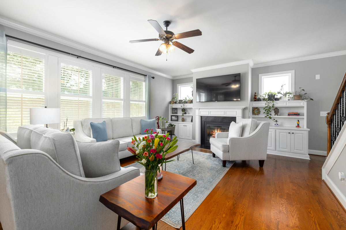 Bright and cozy living room with white sofas, wood floors, a fireplace with built-in shelving, and a large flat-screen TV.