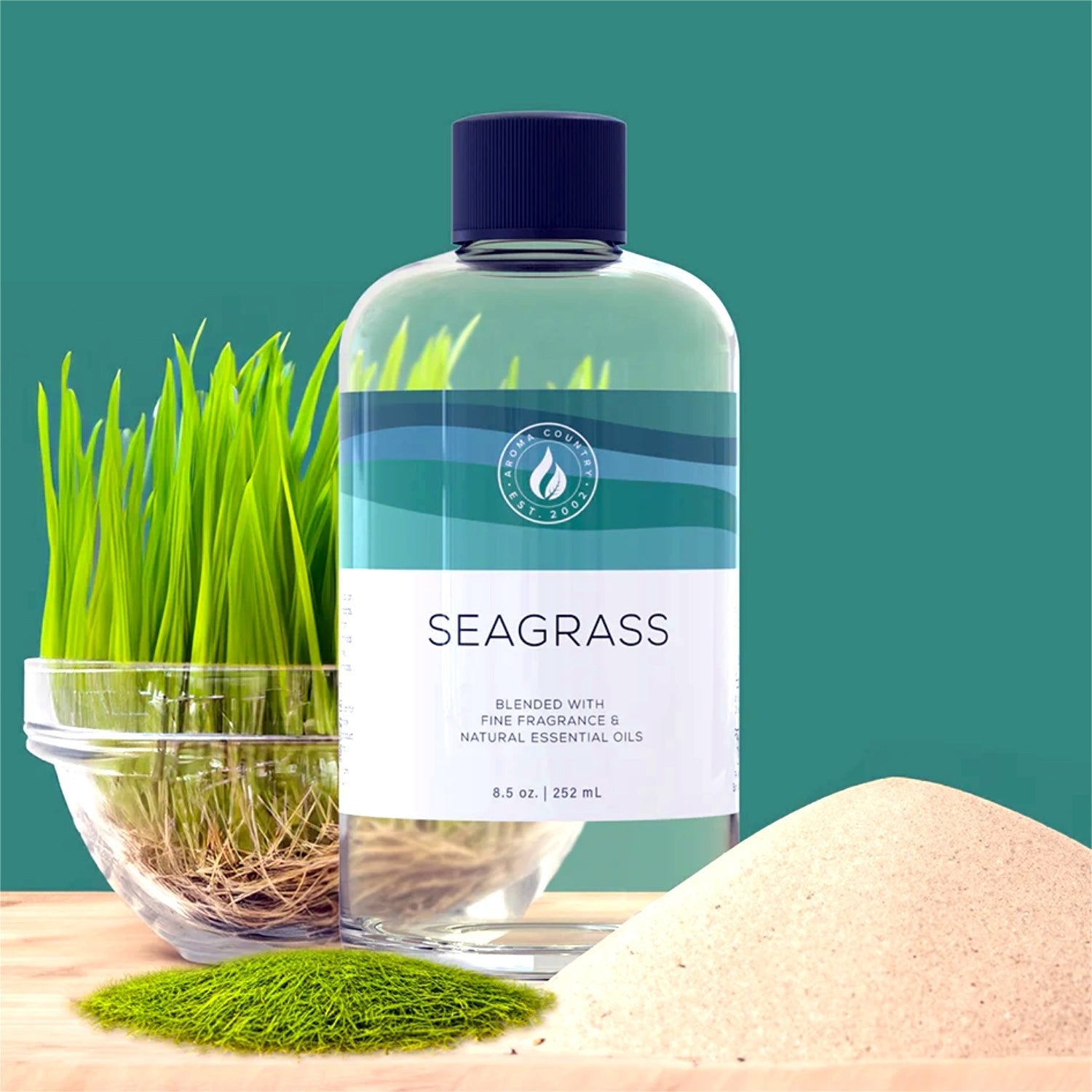 Seagrass diffuser oil 8.5 oz bottle displayed with live seagrass roots and a soft mound of sand, evoking a clean coastal-inspired fragrance.